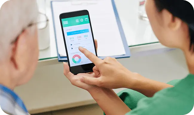 A person in scrubs shows a smartphone with health data and charts to another person, likely a patient, during a consultation—highlighting the benefits of RPM and CCM for ongoing care management.